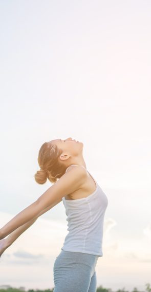 Young beautiful woman raising hands with beautiful view at meadow enjoy fresh air.